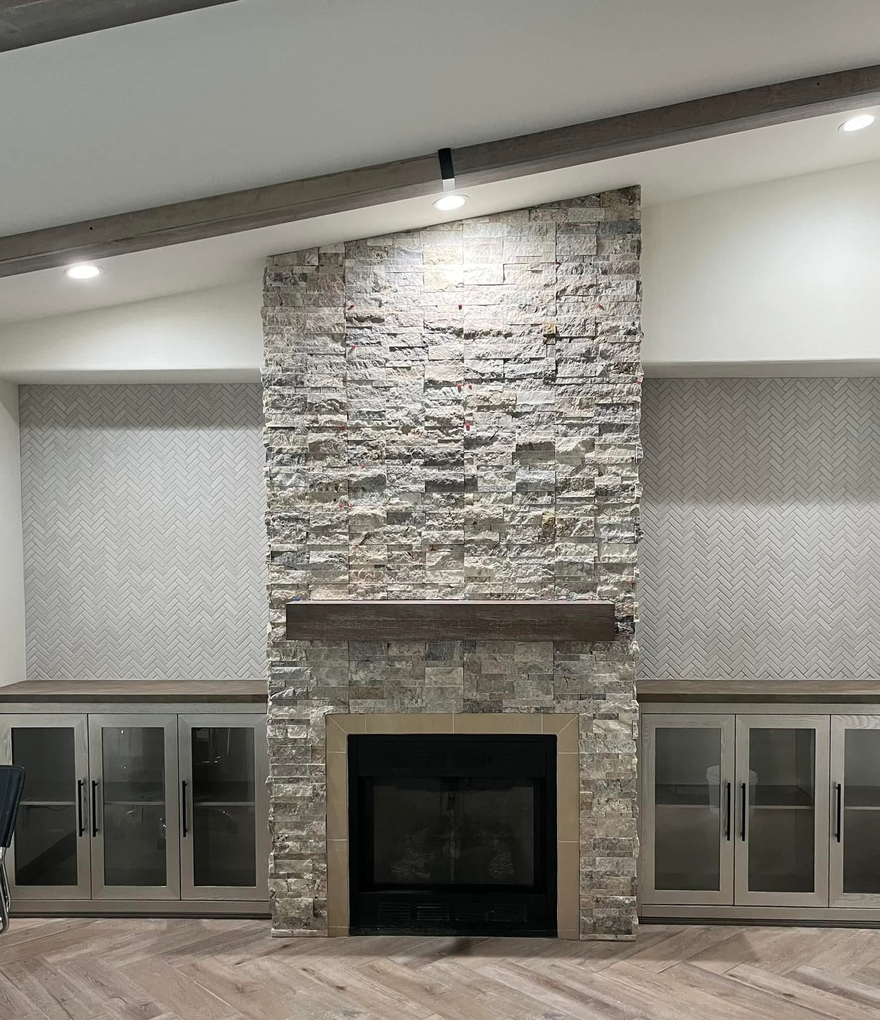 Finished fireplace remodel with stacked stone chimney breast, wood mantel, and herringbone tile
